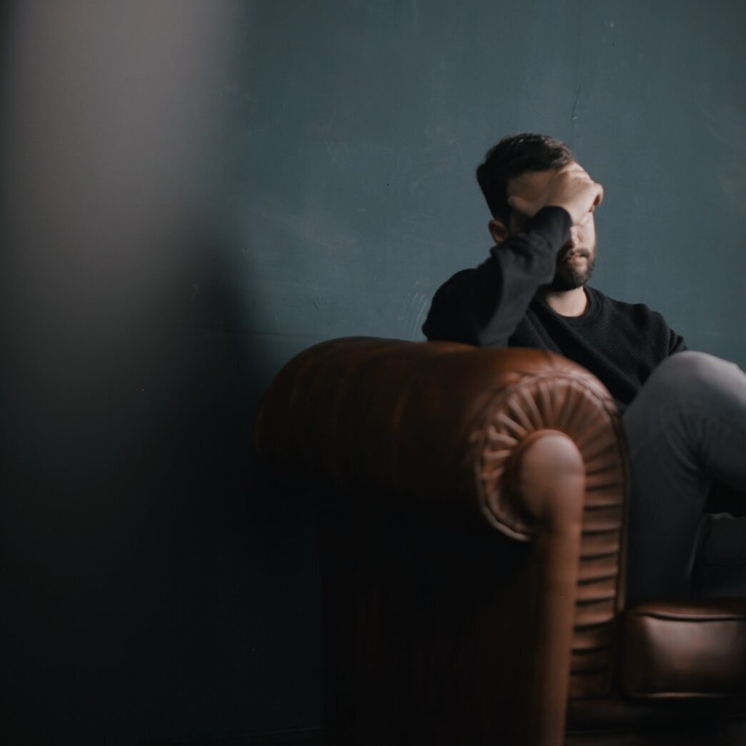 a man holds his head while sitting on a sofa