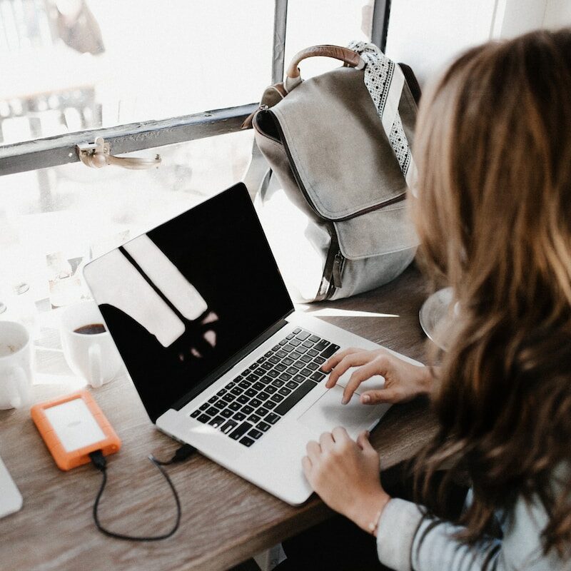 Photo by Andrew Neel girl wearing grey long-sleeved shirt using MacBook Pro on brown wooden table